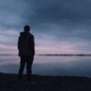 暗い海の前に立ち、自分は無価値なのではと孤独を感じる男性