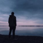 暗い海の前に立ち、自分は無価値なのではと孤独を感じる男性